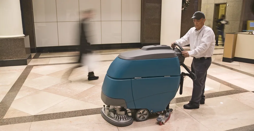 Medewerker reinigt de vloer van een entreehal met een schrobmachine